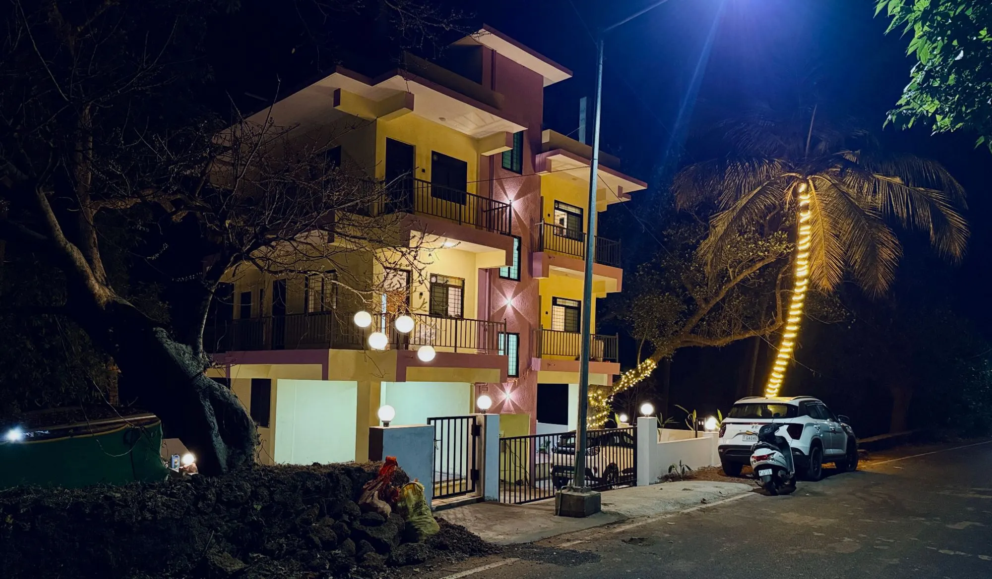 Sadanand Guest House building lit up at night, with a palm tree in fairy lights